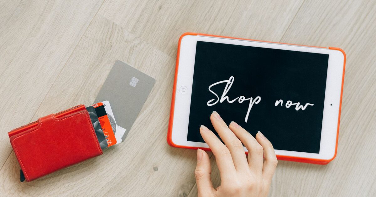 A tablet showing a Shop now button beside a wallet of payment cards, with a hand reaching towards the screen