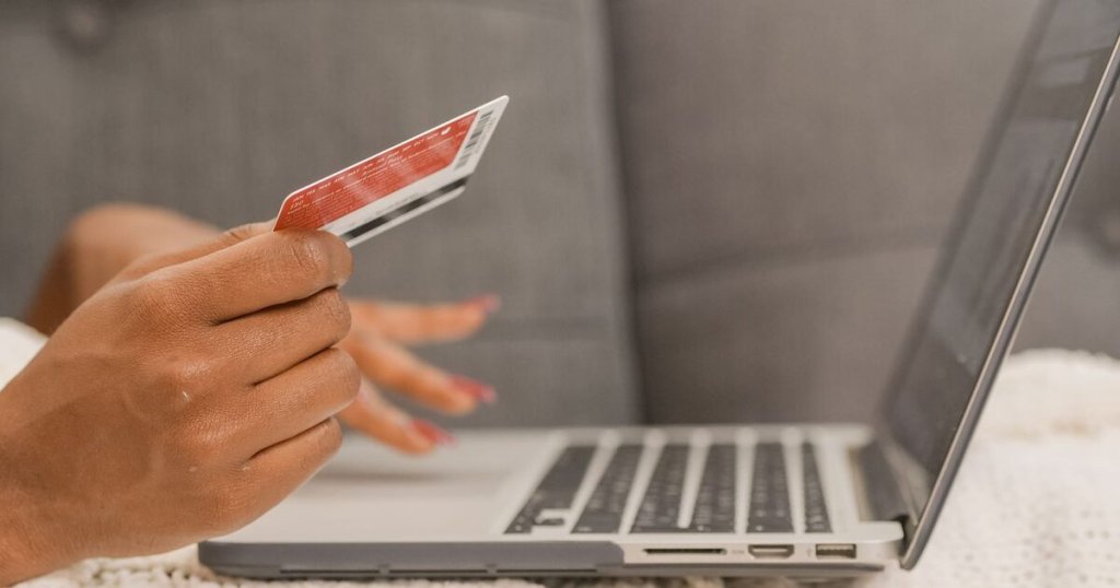A person holding a payment card while shopping online on a laptop