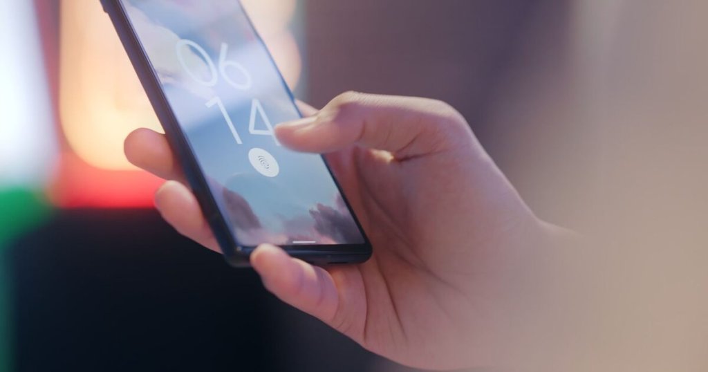 A hand holding a smartphone showing a lock screen with a fingerprint sensor icon
