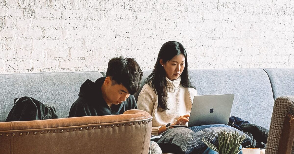 Two people working on laptops on sofas in a coffee shop, the kind of shared public wifi a VPN is useful on